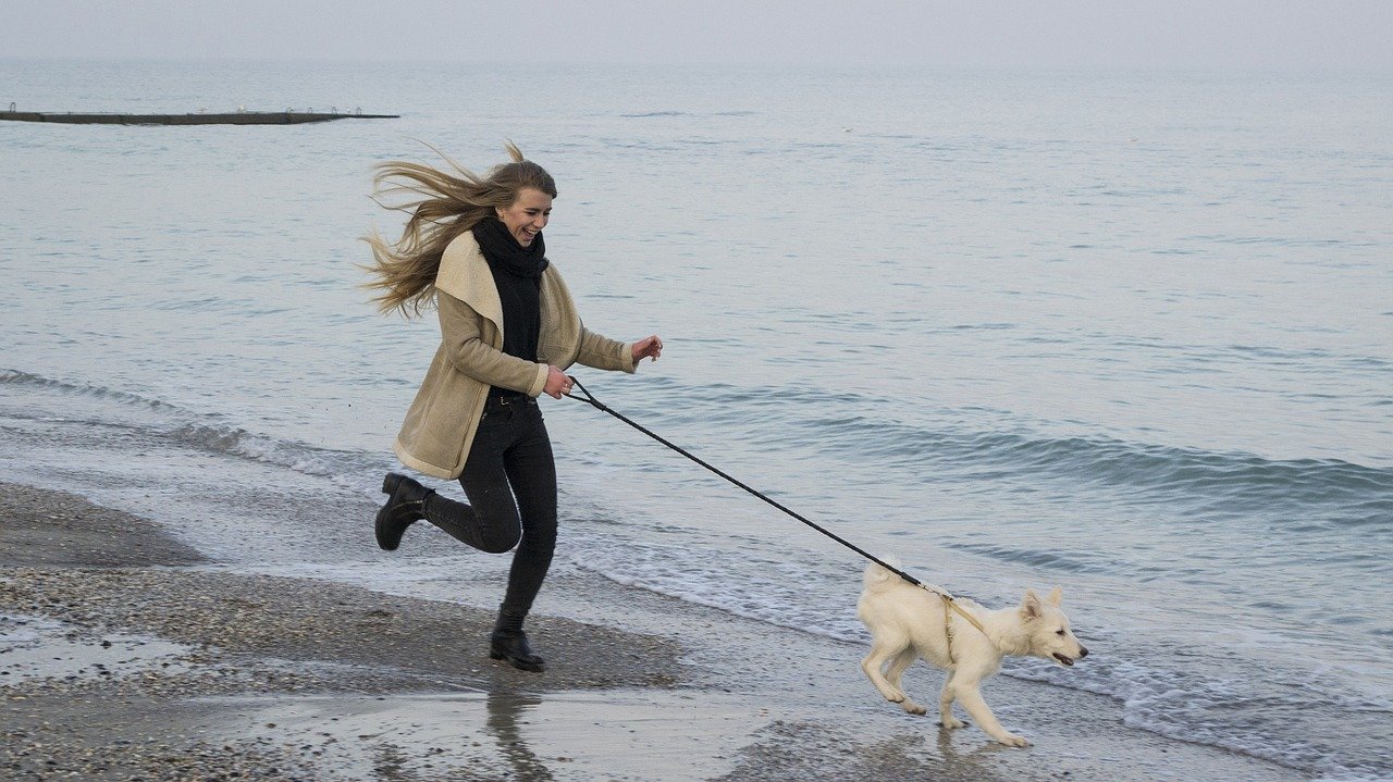 kobieta biega z psem po plaży